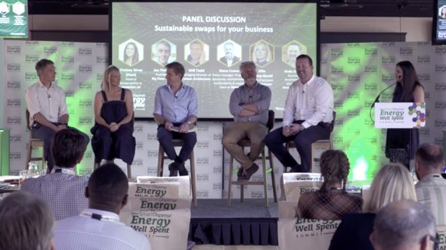 A panel of six individuals, five sitting and one standing, discuss sustainable swaps for business at the "Energy Well Spent Summit." A presentation slide is visible in the background.