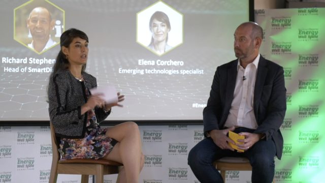 Two individuals, a woman and a man, are seated on stage discussing at an event. Behind them are projected images and the text "Richard Stephens, Head of SmartD" and "Elena Corchero, Emerging technologies specialist".