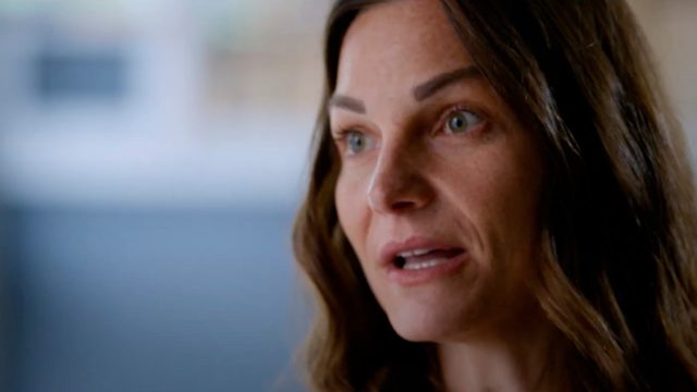 Close-up of a woman with long brown hair, speaking. She has an earnest expression and is looking slightly to the right. The background is softly blurred.